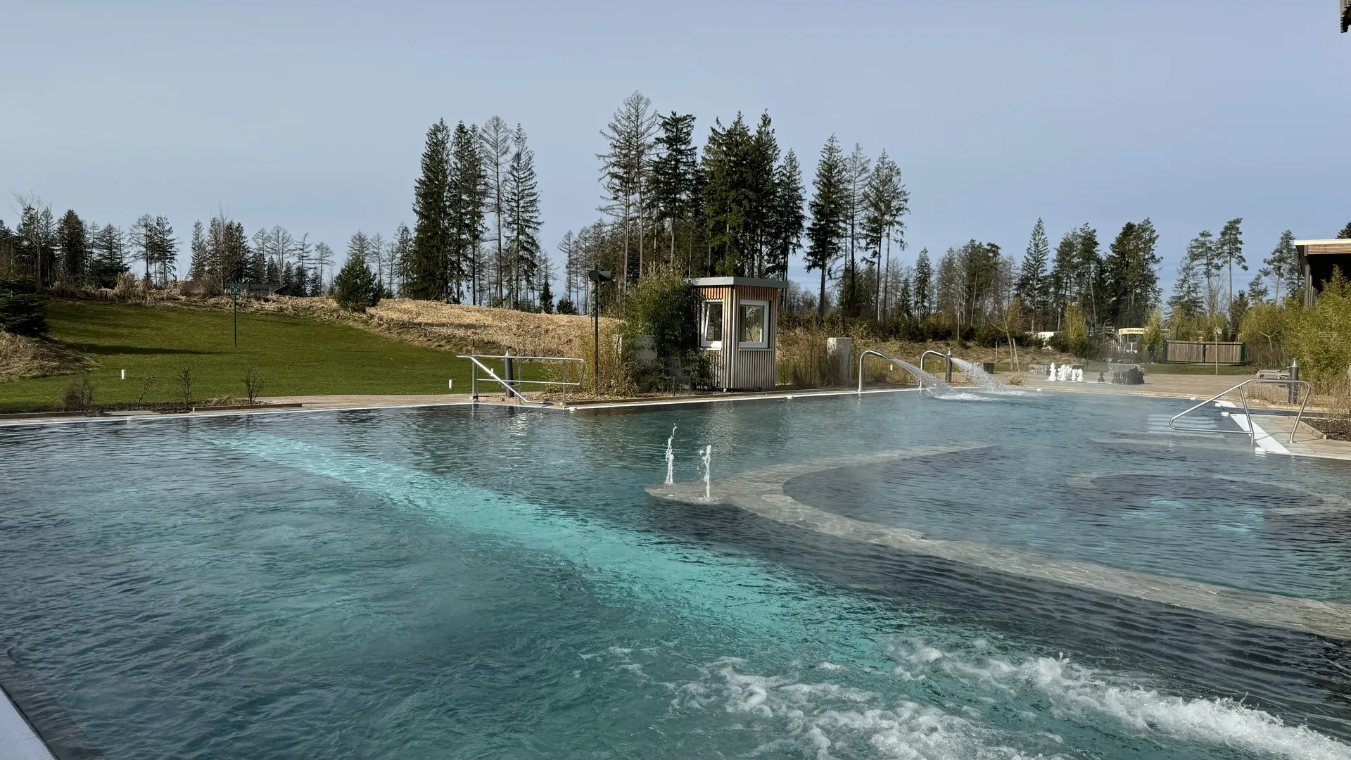 Großes beheiztes Außenbecken des Aqua Mundo Park Allgäu mit Tannen im Hintergrund