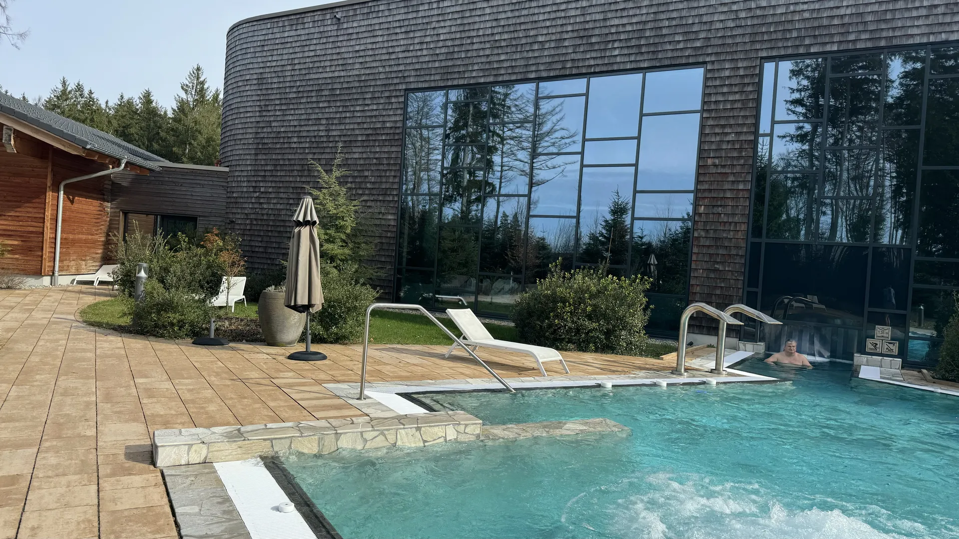 Außenpoolbereich am Deep Nature Spa Park Allgäu mit Liegen und Holzfassade des Hauptgebäudes