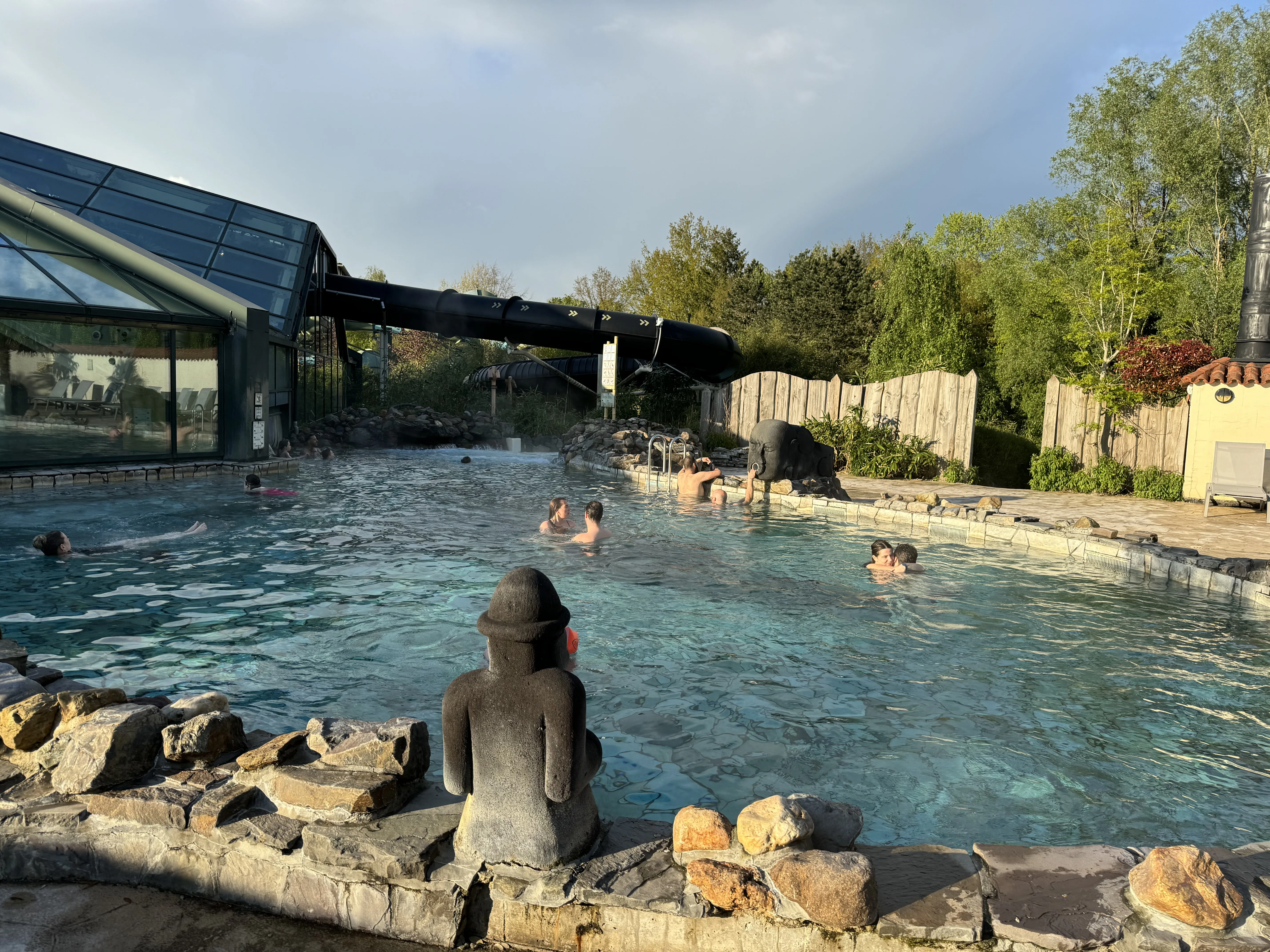 Das Außenbecken aus einer anderen Perspektive – mit asiatischen Steinfiguren und der schwarzen Wildwasserbahn im Hintergrund