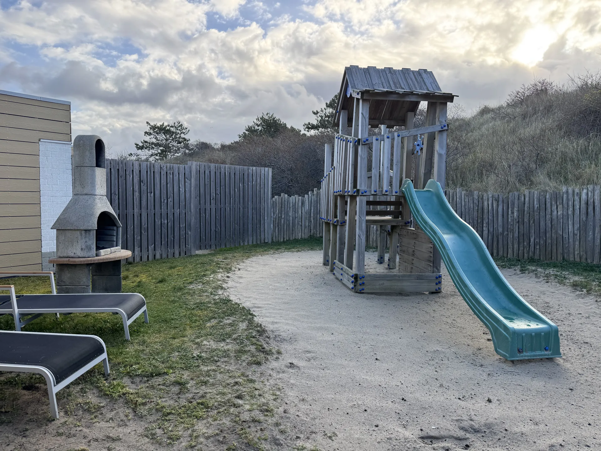 Eingezäunter Garten mit Spielturm, türkiser Rutsche, gemauertem Grill und Sonnenliegen