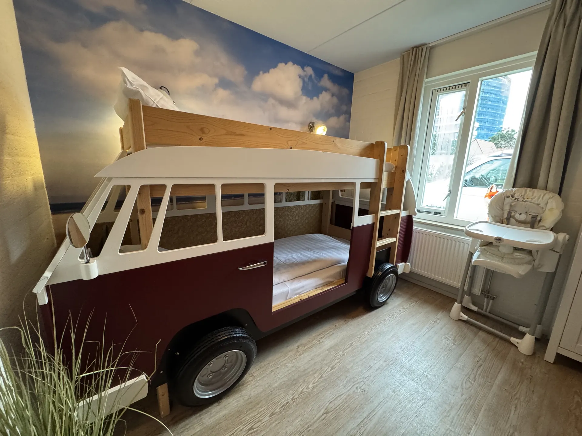 Kinderzimmer mit VW-Bus-Stockbett in Weinrot und Weiß, Wolken-Fototapete, daneben ein Kinderhochstuhl