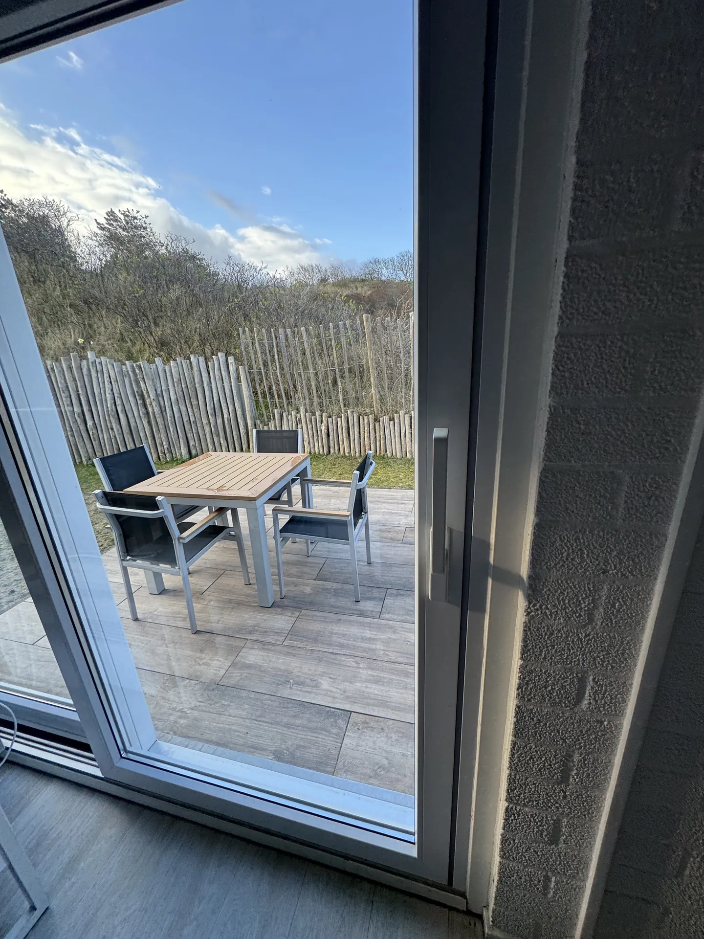 Blick von der Terrasse durch die Fenstertür auf die Dünen und den Nachbargarten