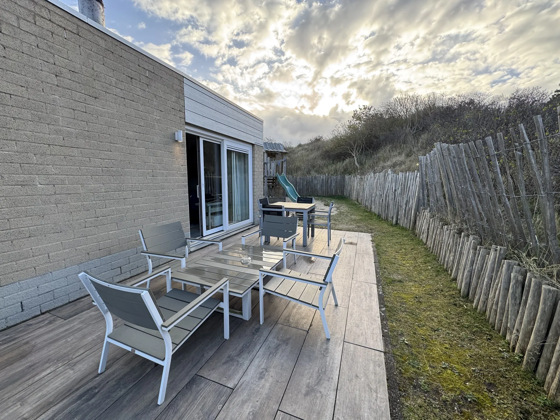 Terrasse mit Sitzgruppe und Liegen, Blick auf die Dünenlandschaft und Holzzaun