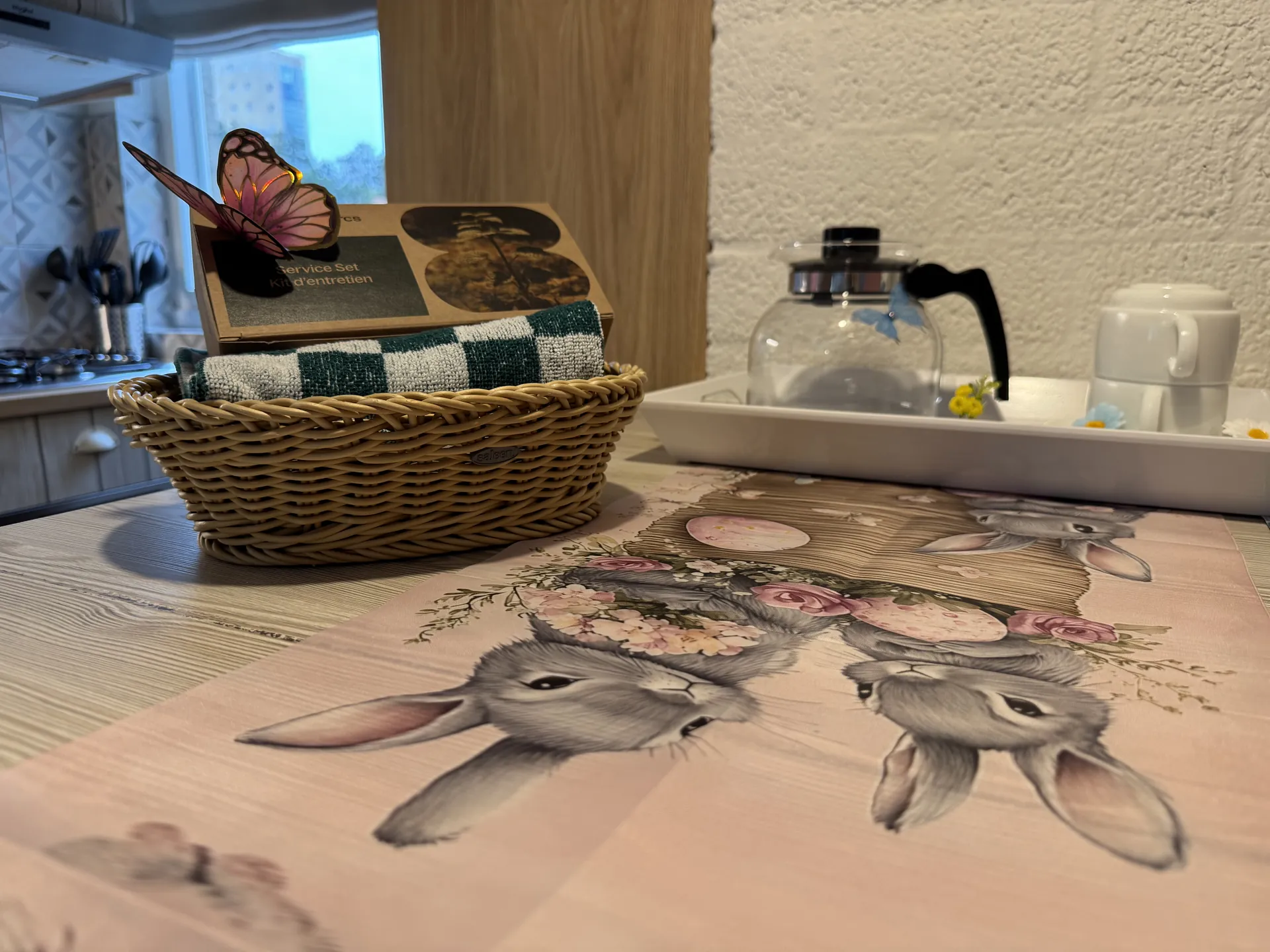 Willkommenskorb auf dem Esstisch mit Geschirrtuch und Karte, dahinter Kaffeekanne