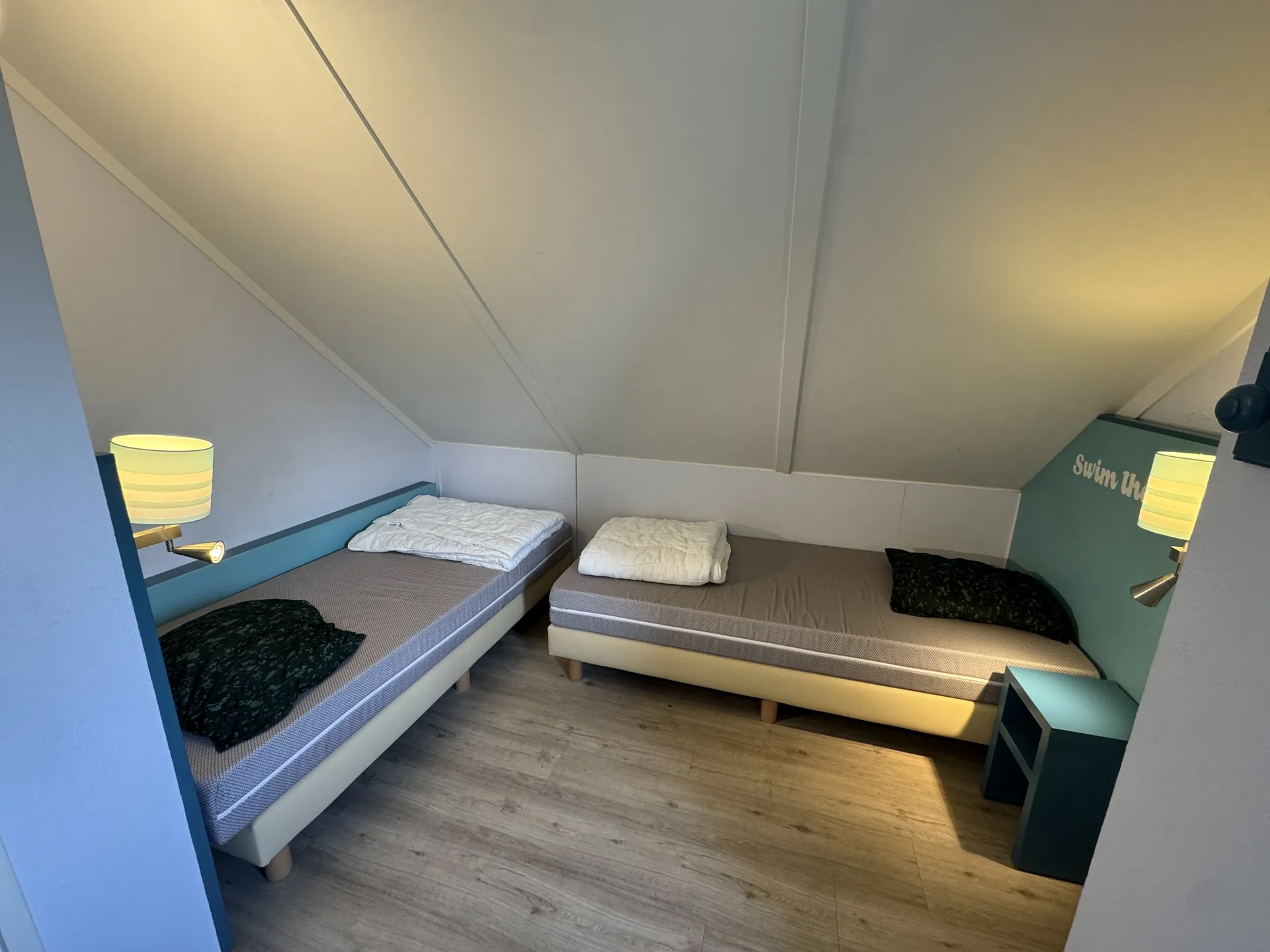 Kinderzimmer unter der Dachschräge mit zwei Einzelbetten und Nachttischlampen