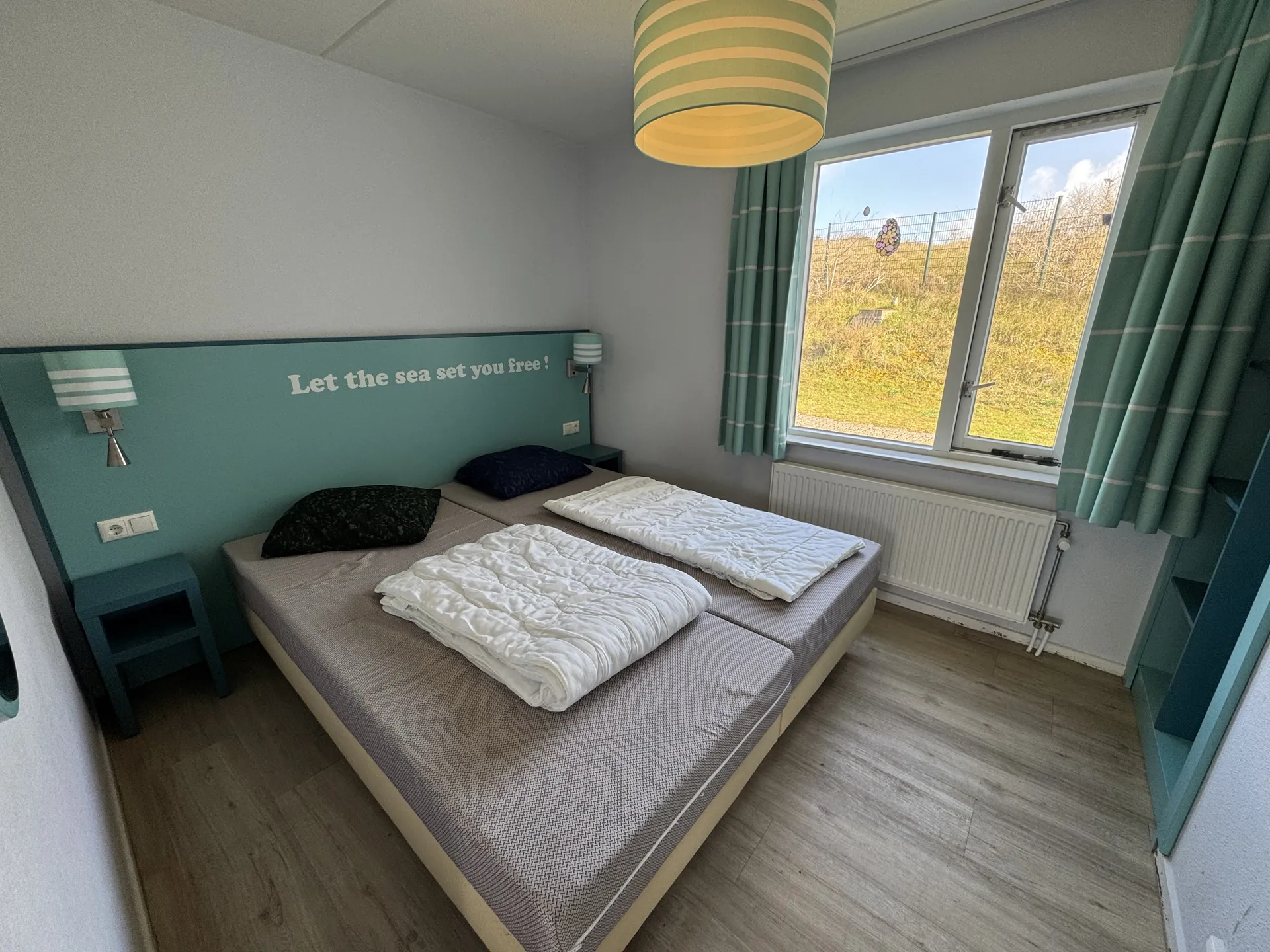 Schlafzimmer im Erdgeschoss mit Doppelbett und Blick auf Dünenlandschaft durch das Fenster