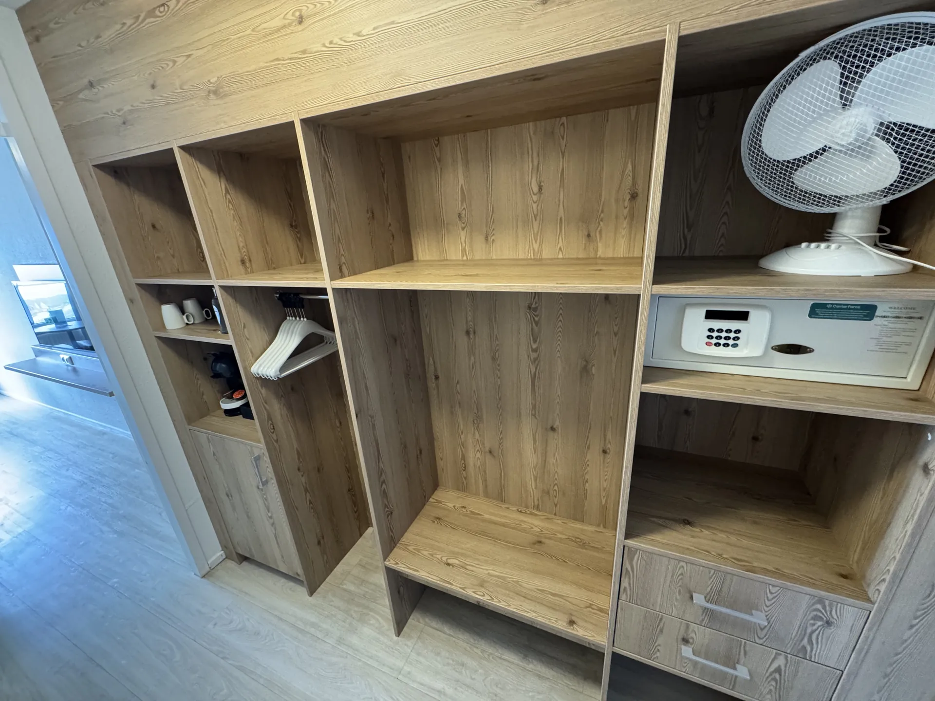 Offener Schrankbereich mit Holzfächern, Kleiderbügeln und Safe