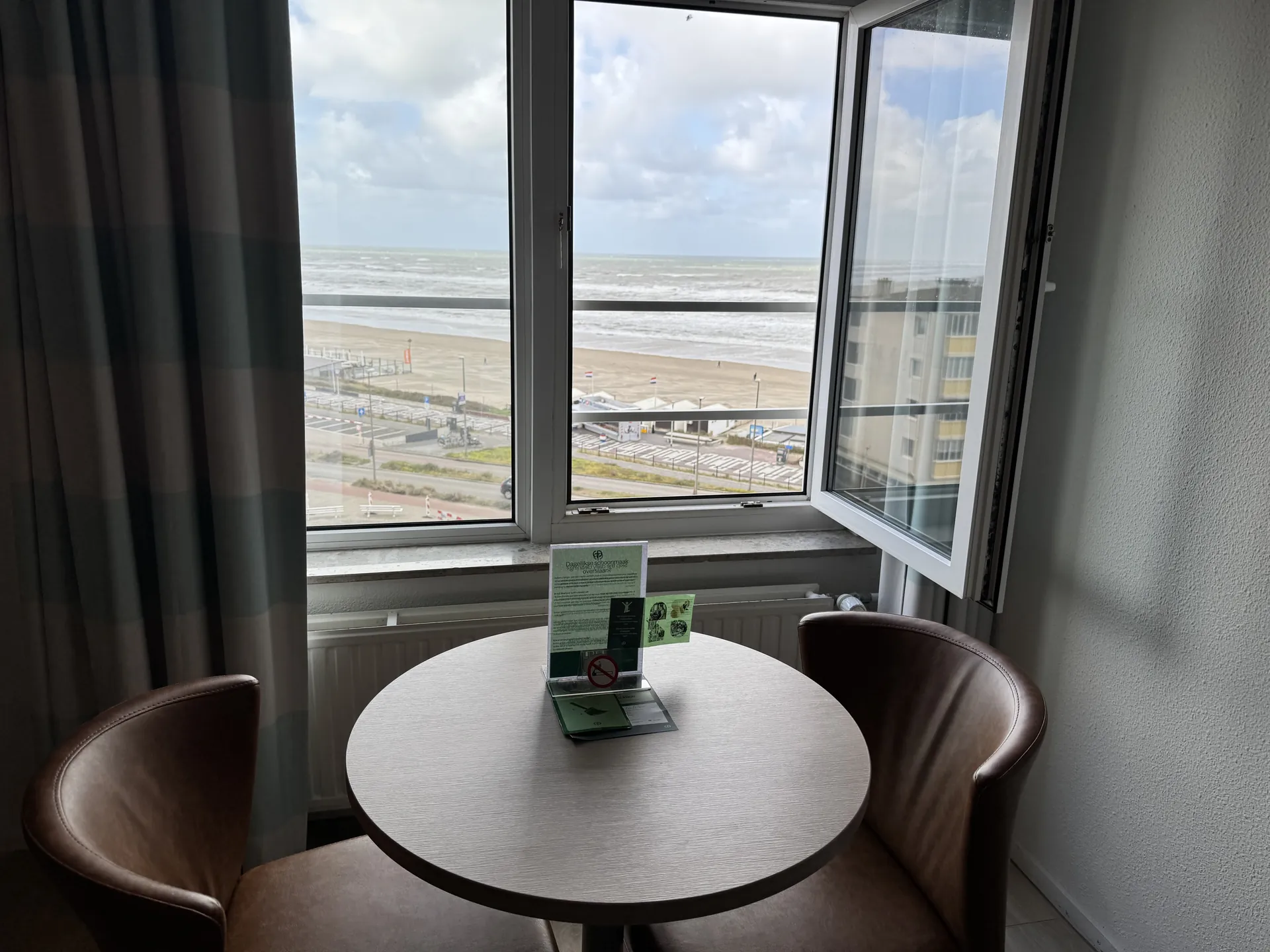 Sitzecke am Fenster mit kleinem Rundtisch, zwei Lederstühlen und Blick auf Strand und Nordsee