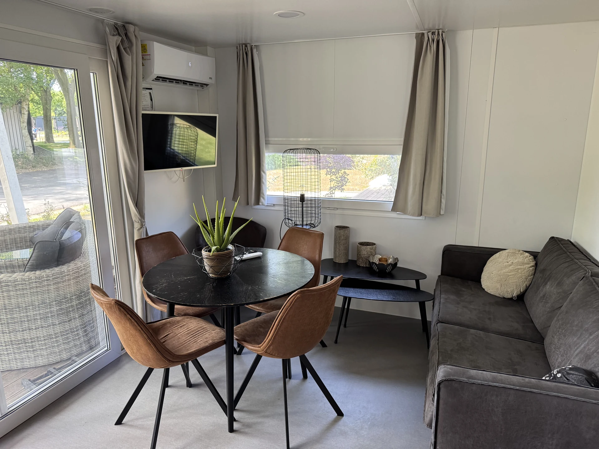 Ess- und Wohnbereich eines kompakteren Chalets im EuroParcs Kaatsheuvel mit rundem Tisch, Lederstühlen, Sofa und Klimaanlage