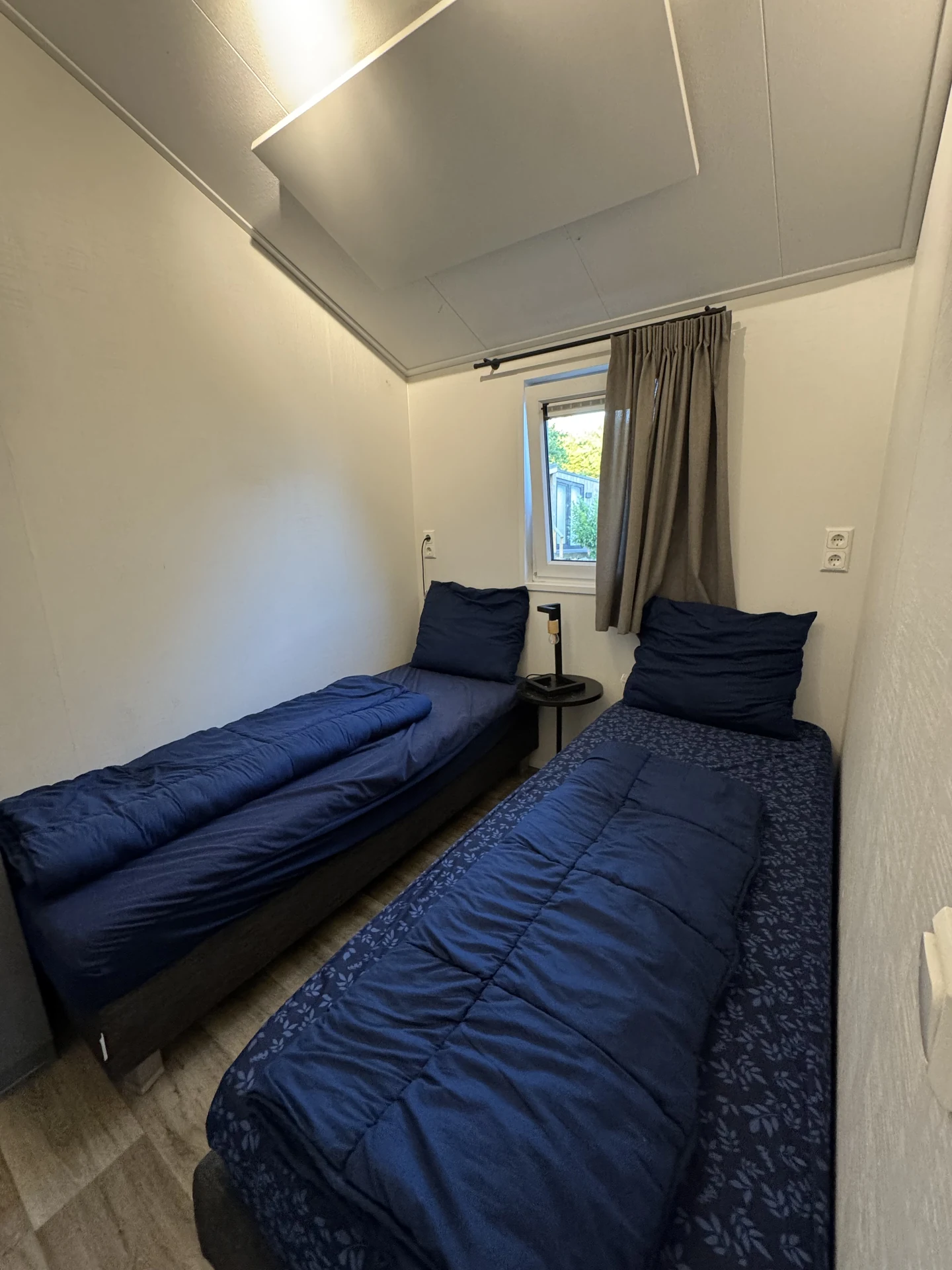 Schlafzimmer in einem Chalet im EuroParcs Kaatsheuvel mit zusammengestellten Einzelbetten, dunkelblauer Bettwäsche und Einbauschrank