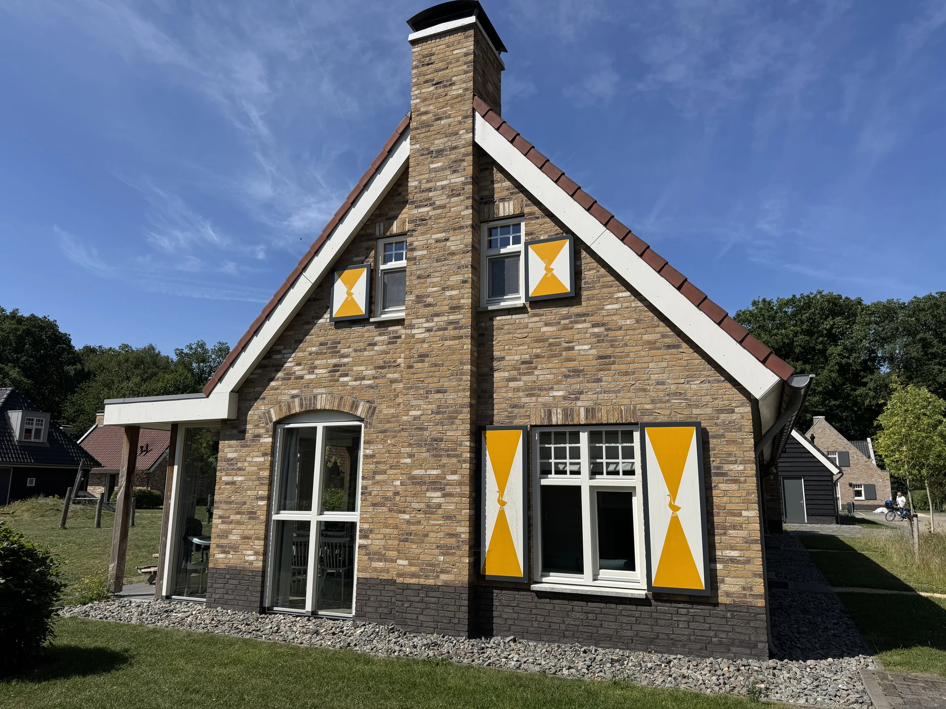 Giebelseite eines Ferienhauses im Landal Kaatsheuvel aus Backstein mit gelb-weißen Fensterläden und überdachter Terrasse