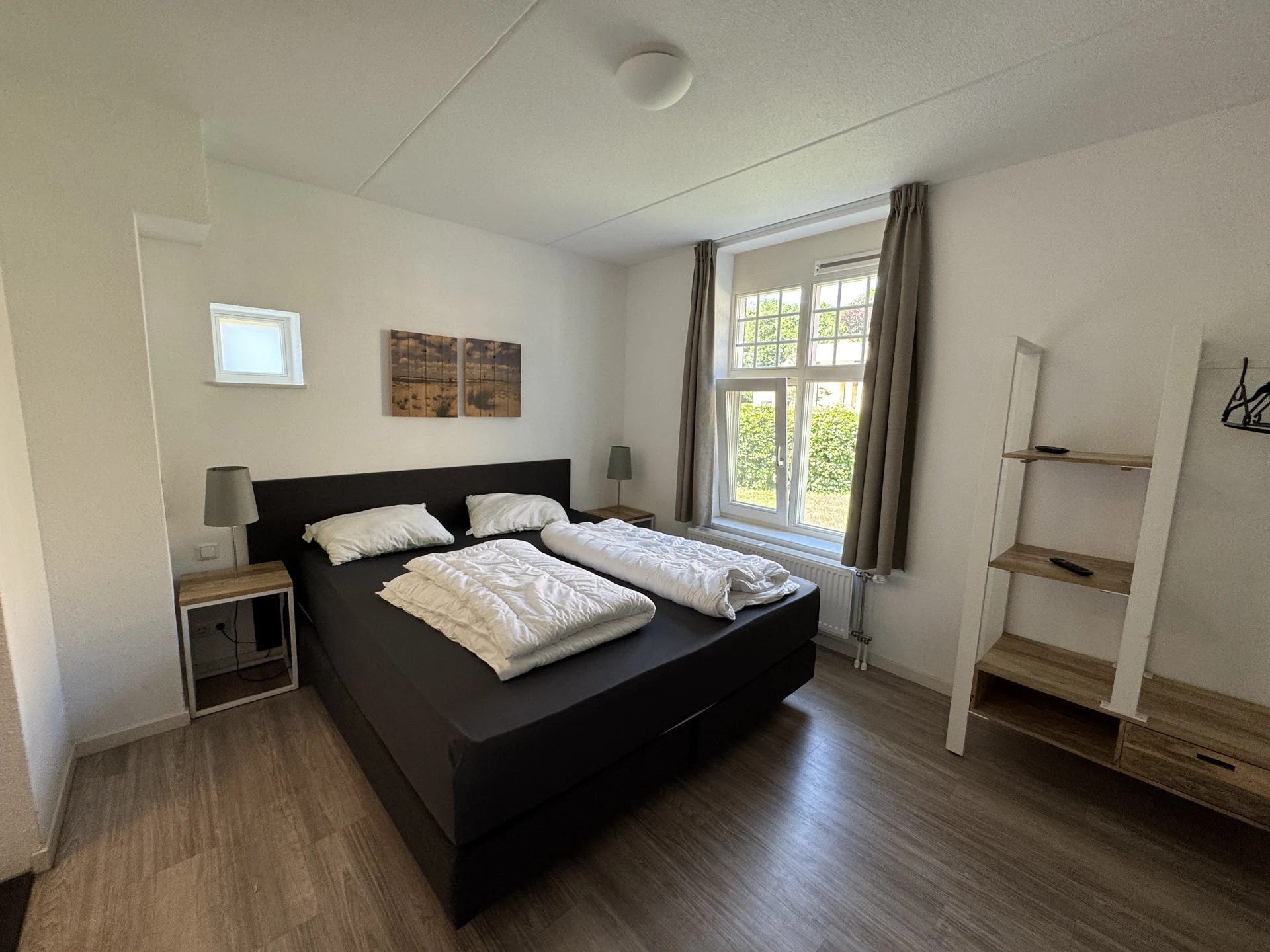 Schlafzimmer in einem Ferienhaus im Landal Kaatsheuvel mit Boxspringbett, Holznachttischen und Dünenbildern an der Wand