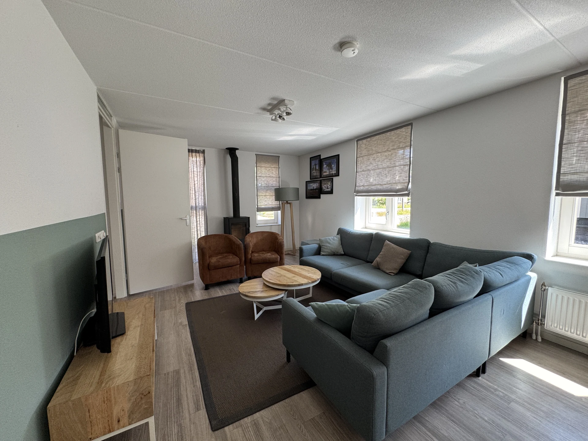 Wohnzimmer eines Ferienhauses im Landal Kaatsheuvel mit großem grüngrauem Ecksofa, zwei braunen Ledersesseln und schwarzem Kaminofen