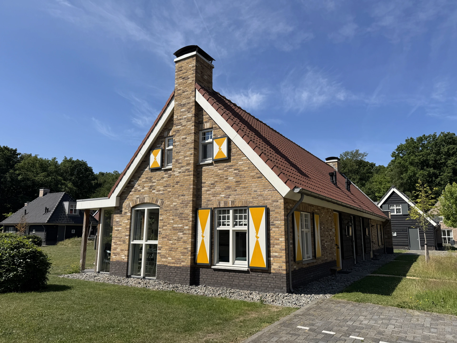 Ferienhaus im Landal Kaatsheuvel aus hellem Backstein mit rotem Ziegeldach, Backsteinkamin und gelb-weißen Fensterläden