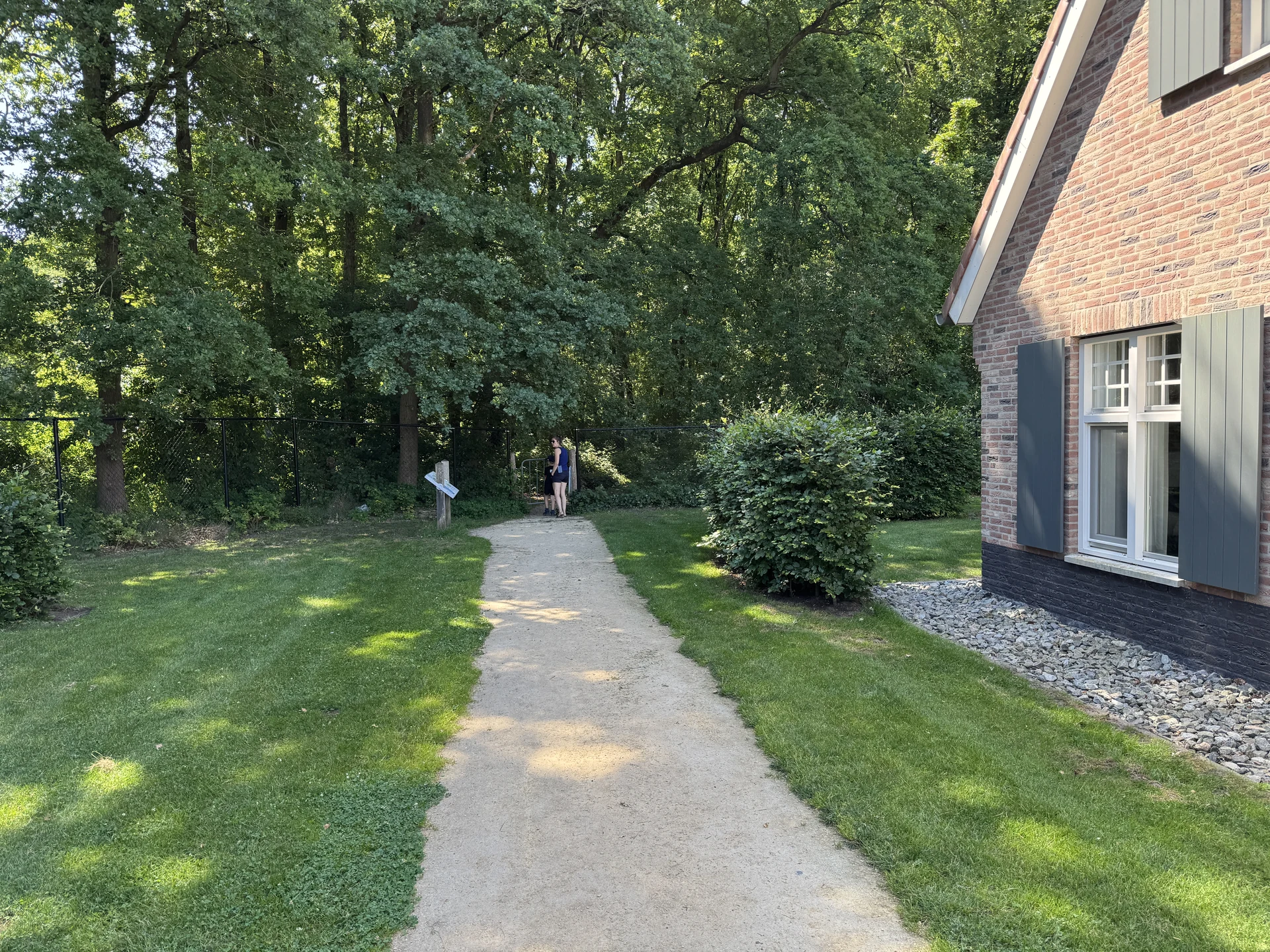 Sandweg zwischen den Ferienhäusern im Landal Kaatsheuvel, der auf ein Tor im Zaun und direkt in den Wald des Nationalparks zuführt