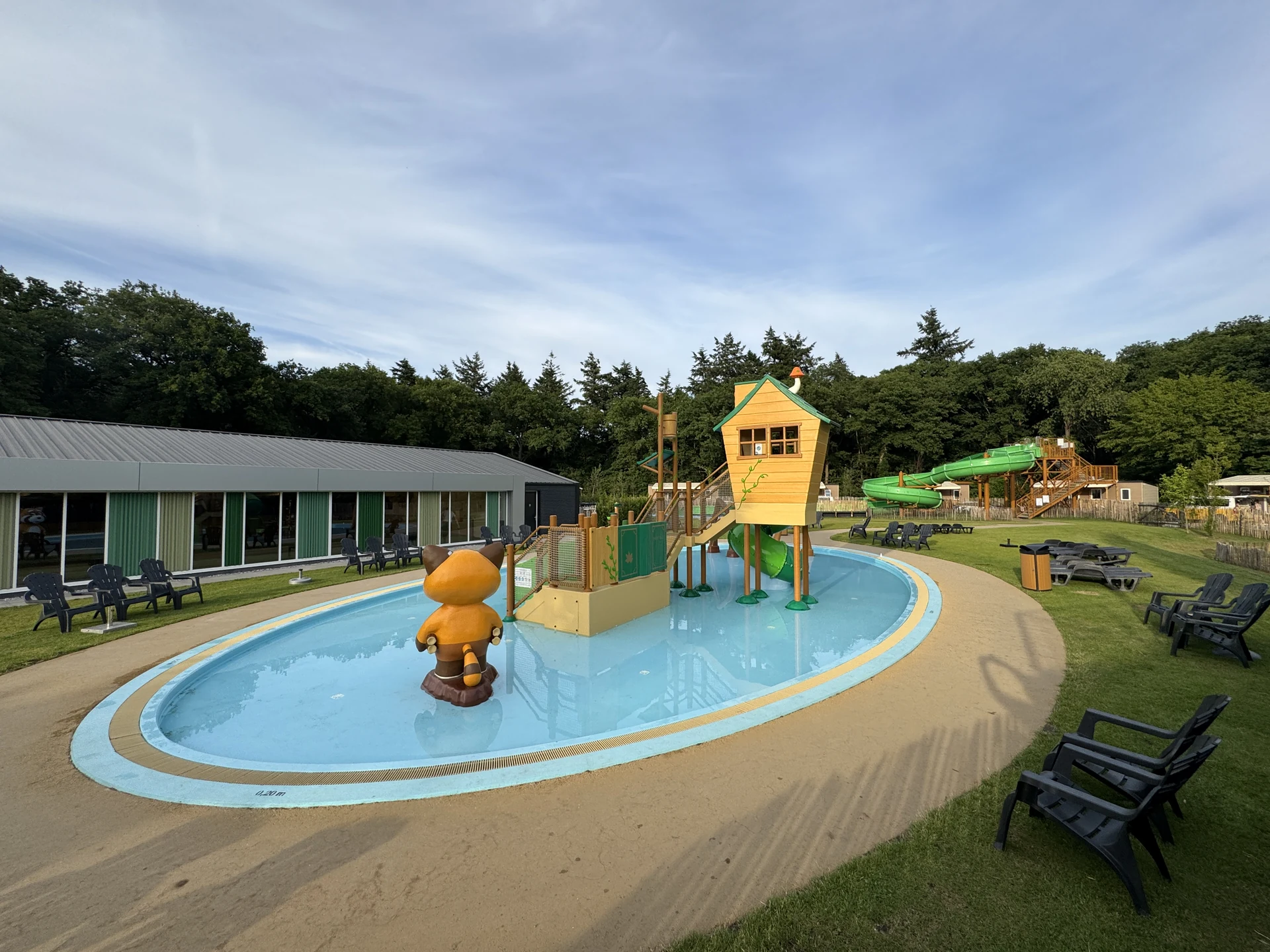 Freibad im Marvilla Parks Kaatsheuvel mit flachem Kinderbecken, hölzerner Wasserspiel-Hütte auf Stelzen und grüner Röhrenrutsche im Hintergrund