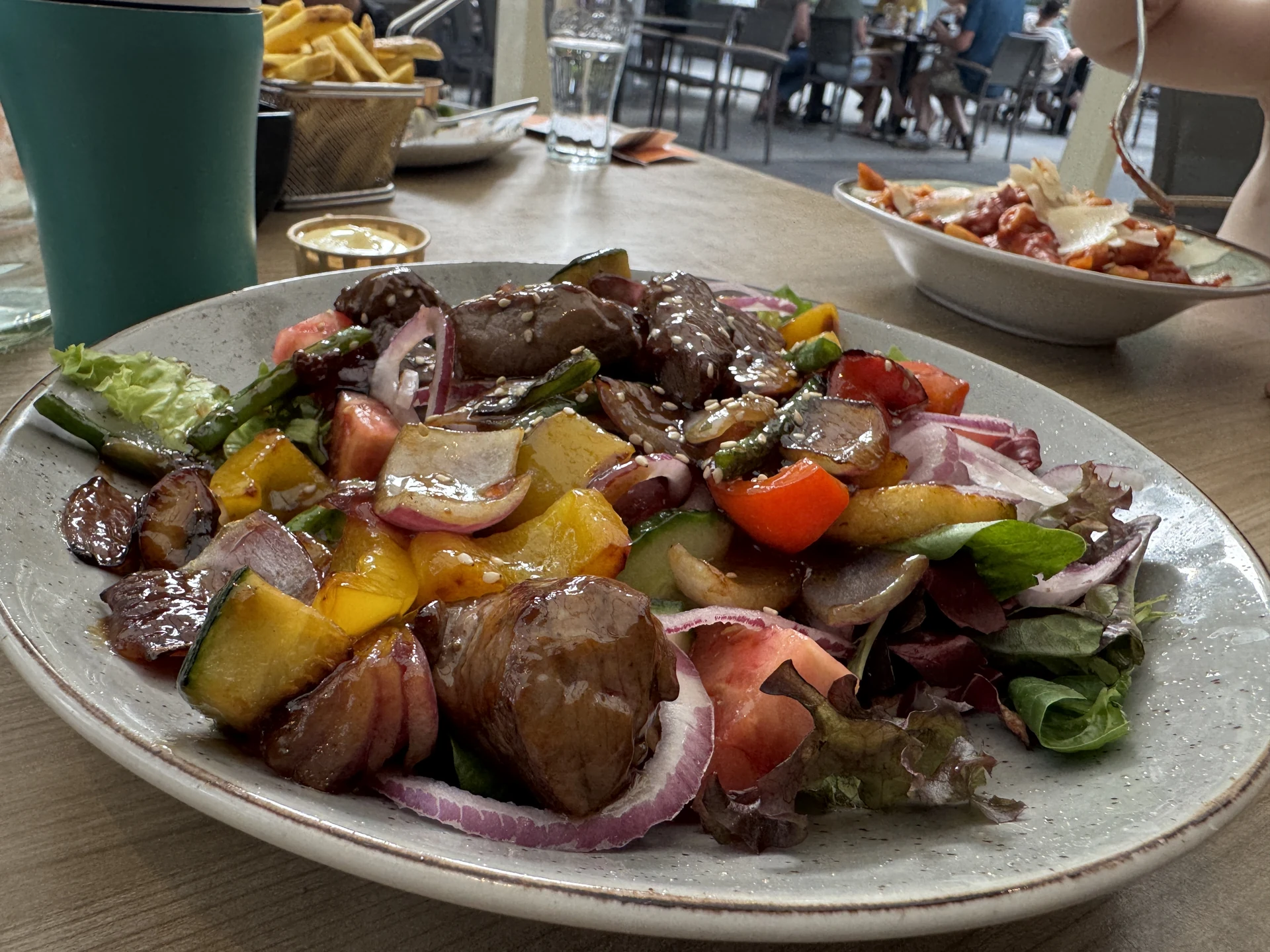 Teller mit Rumpsteak-Salat und gebratenen Kartoffeln im Café Restaurant de Roestelberg, dahinter ein Korb Fritten und eine Schüssel Pasta