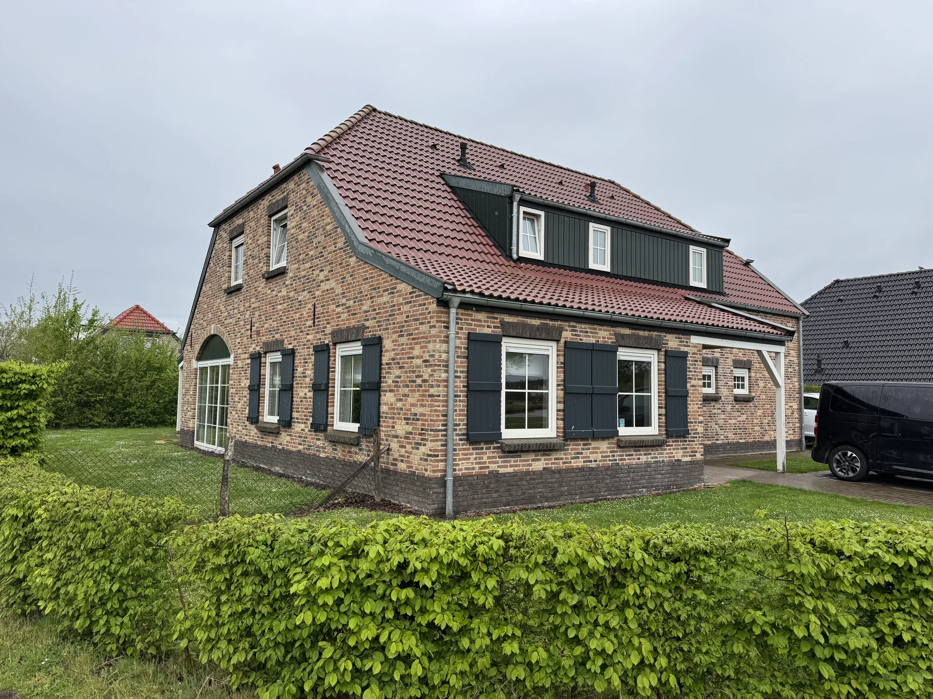 Bauernhaus aus Backstein mit grünen Fensterläden, Hecke und Garten