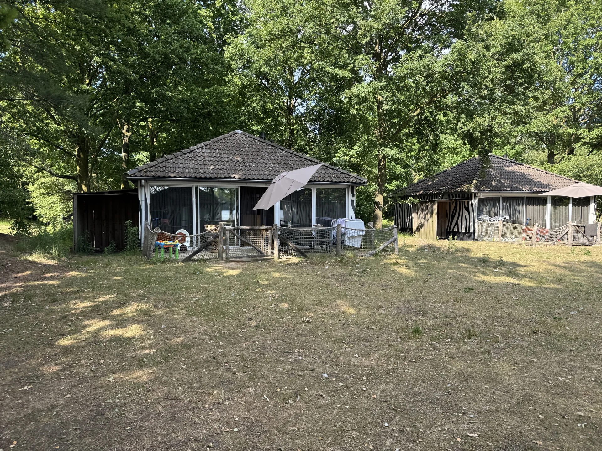 Zwei Bungalows mit Zebra-Fassade im Lake Resort Beekse Bergen, davor eingezäunte Terrassen mit Sonnenschirmen und Kinderspielzeug