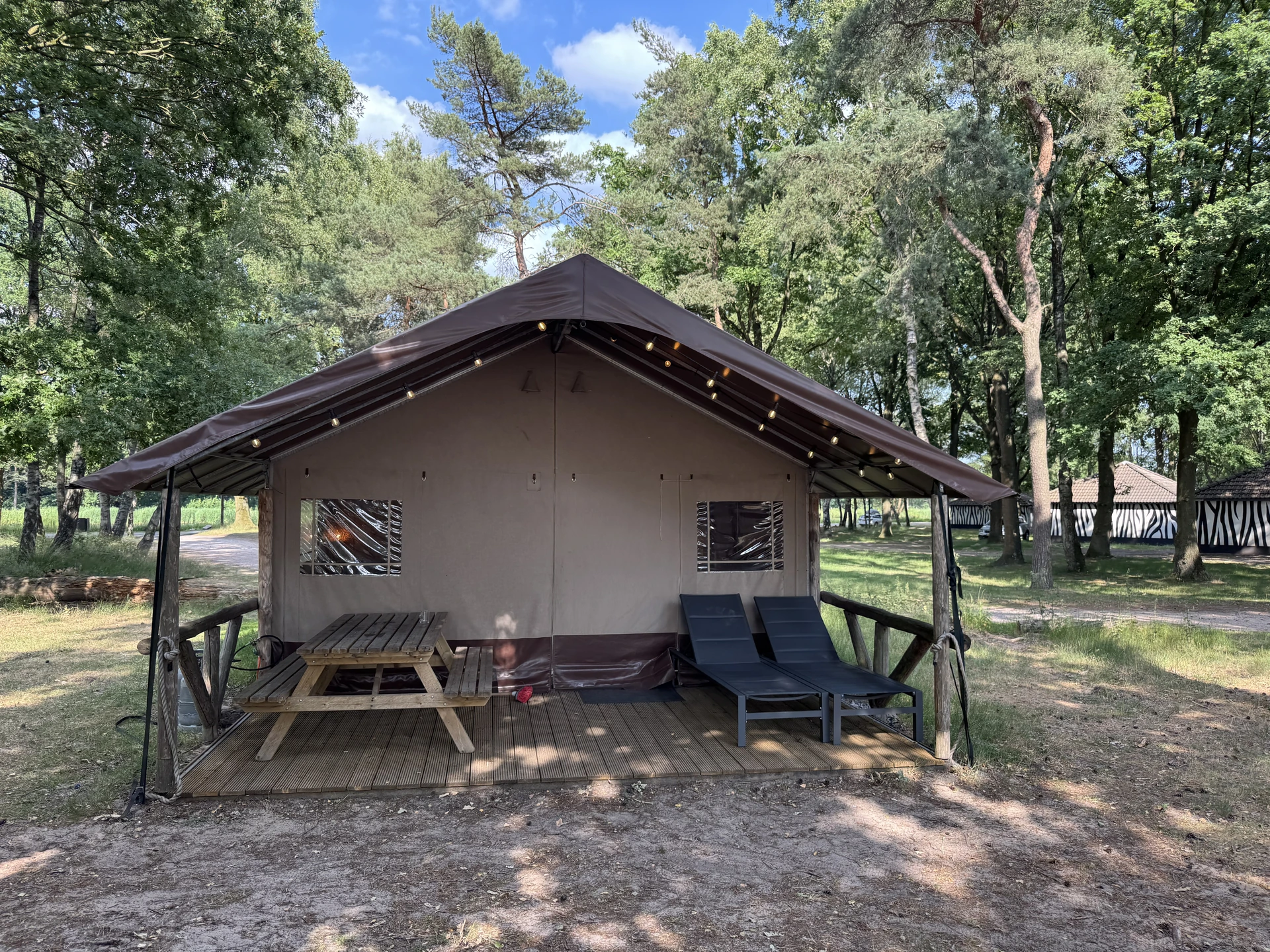Safari-Zelt im Lake Resort Beekse Bergen mit überdachter Veranda, Picknicktisch und Loungesesseln auf Holzplattform