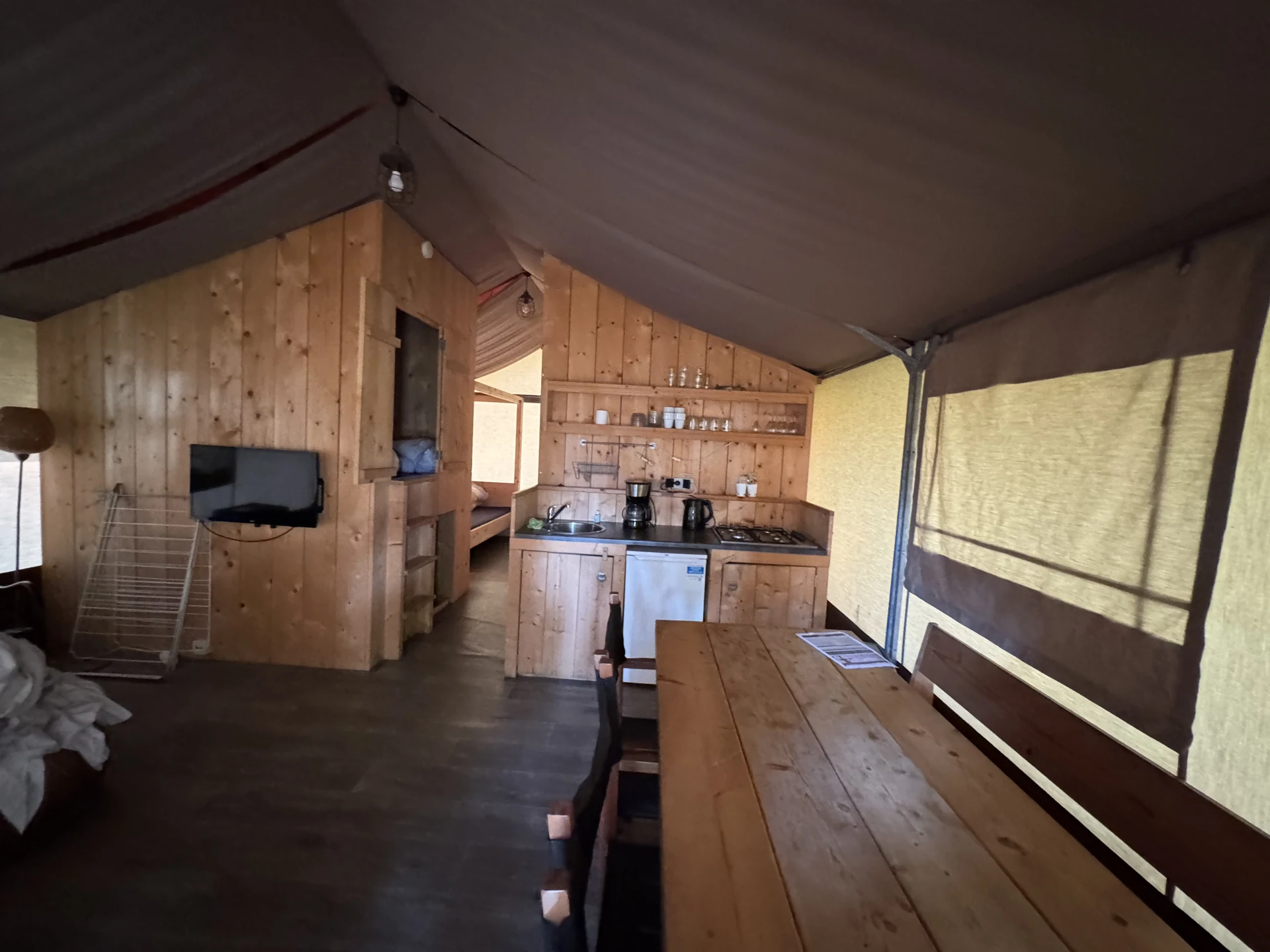 Innenraum eines Safari-Zelts im Lake Resort Beekse Bergen mit langem Holz-Esstisch, Küchenzeile mit Gasherd und Kühlschrank sowie Fernseher