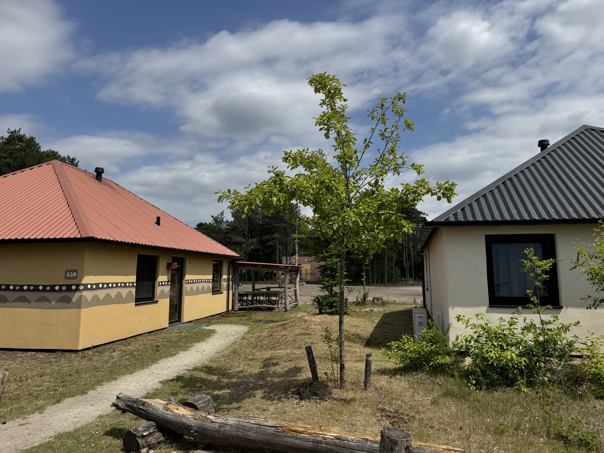 Zwei afrikanisch bemalte Ferienhäuser im Safari Resort Beekse Bergen mit ockerfarbenen Wänden und Ziermuster-Fries, dazwischen ein Sandweg