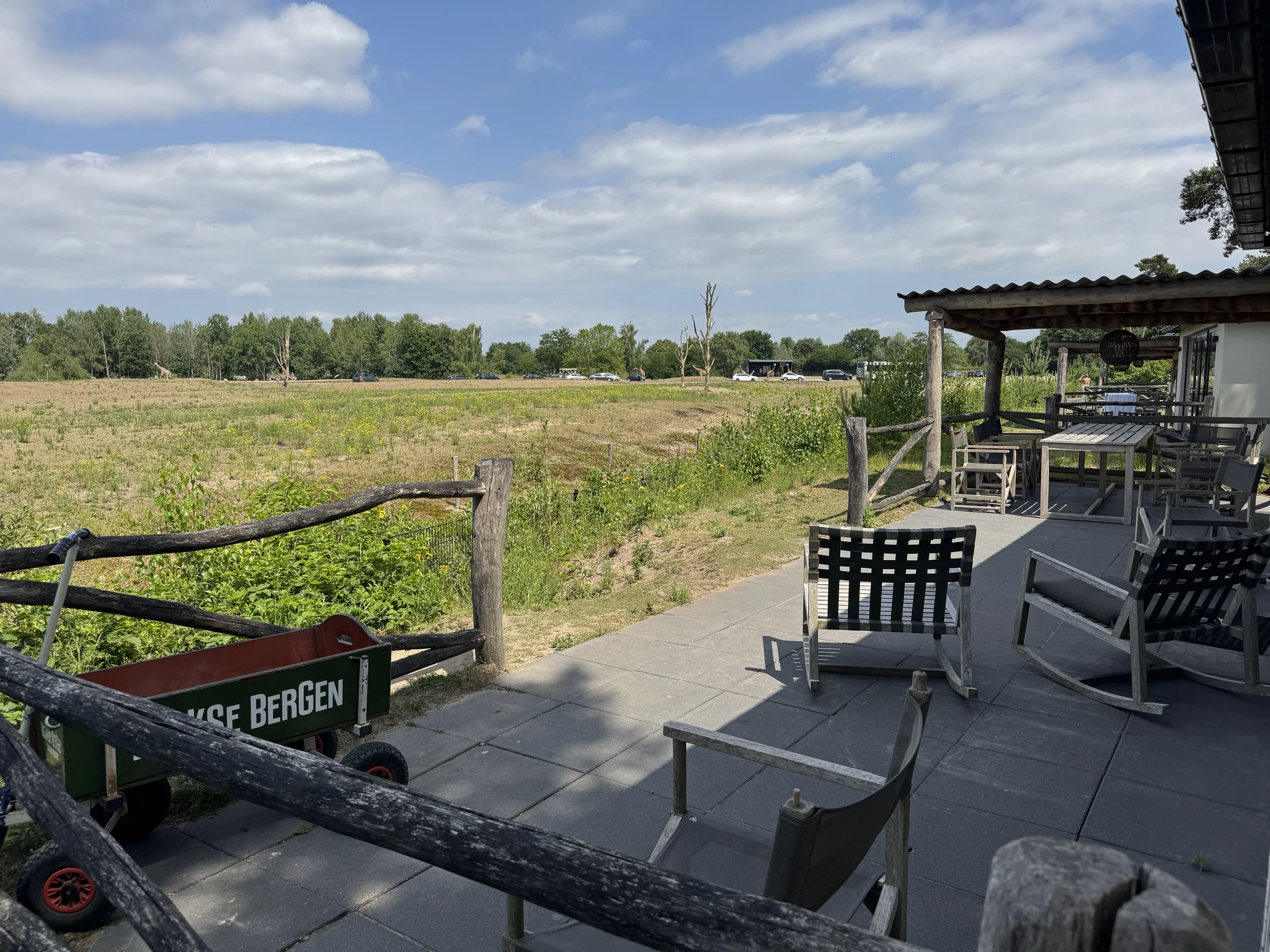 Privatterrasse einer Lodge im Safari Resort Beekse Bergen mit Schaukelstühlen und Holzzaun, dahinter die Savanne mit Giraffen und Nashörnern