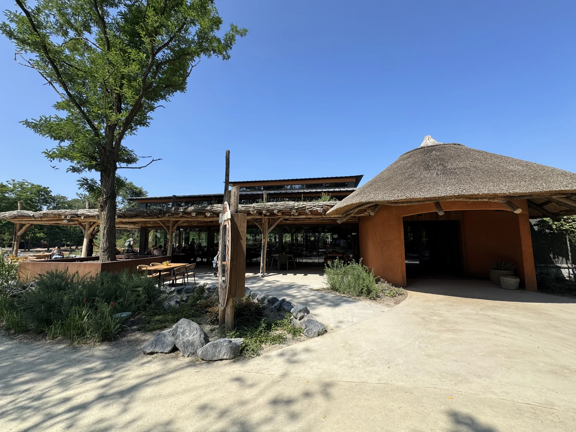 Restaurant mit Reetdach und ockerfarbenen Lehmwänden im Safaripark Beekse Bergen, davor eine offene Terrasse mit Tischen