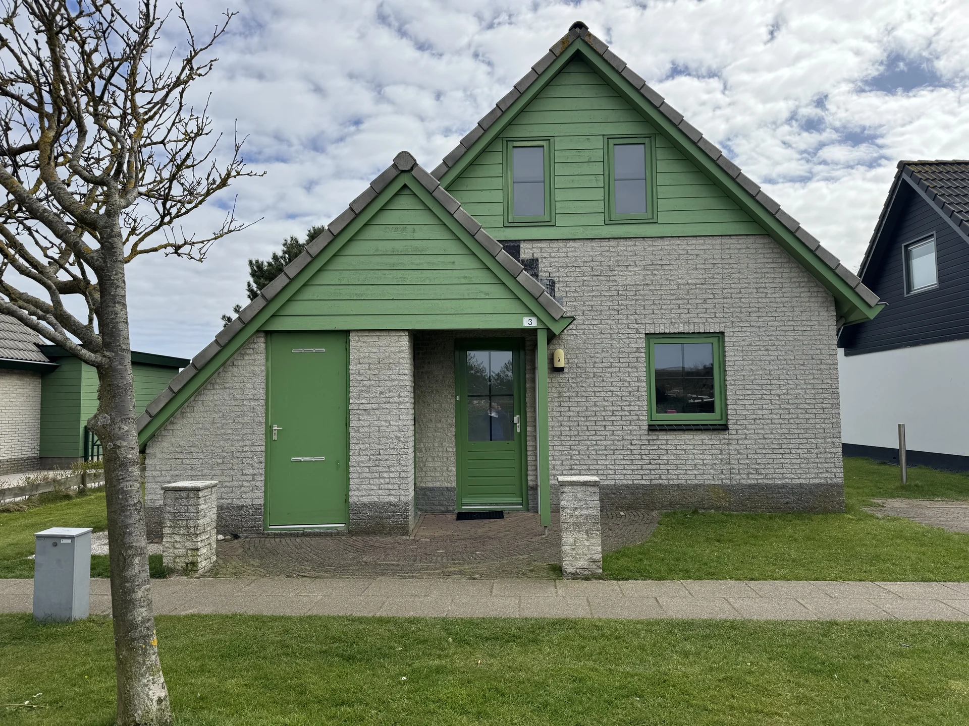 Bungalow im Strandslag mit grüner Holzverkleidung und Vordach