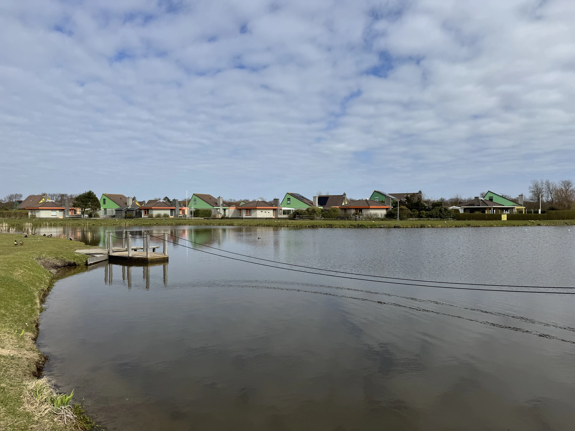 Teich im Bungalowpark Strandslag mit Steg, Seilbahn-Seil und bunten Bungalows am Ufer